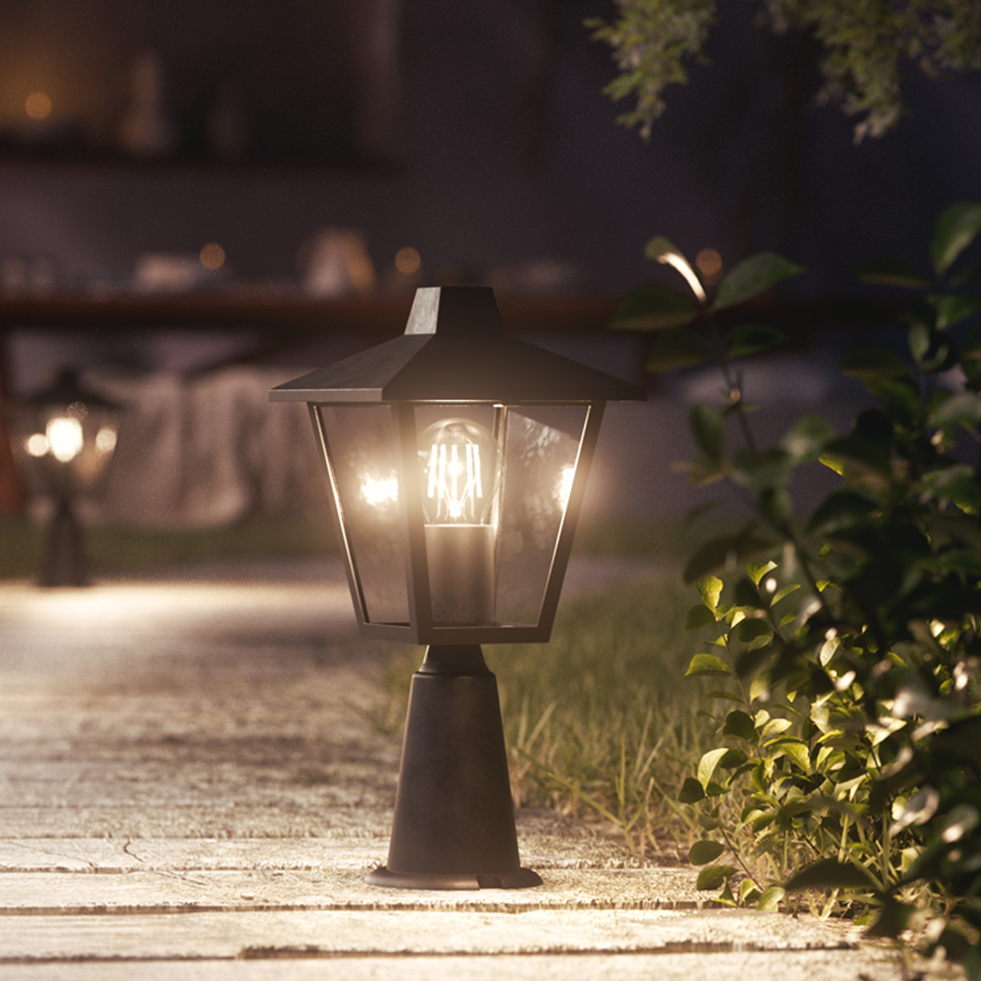 Een zwarte tuinlamp schijnt warm licht op een tuinpad, omringd door groen loof en een vage avondachtergrond.
