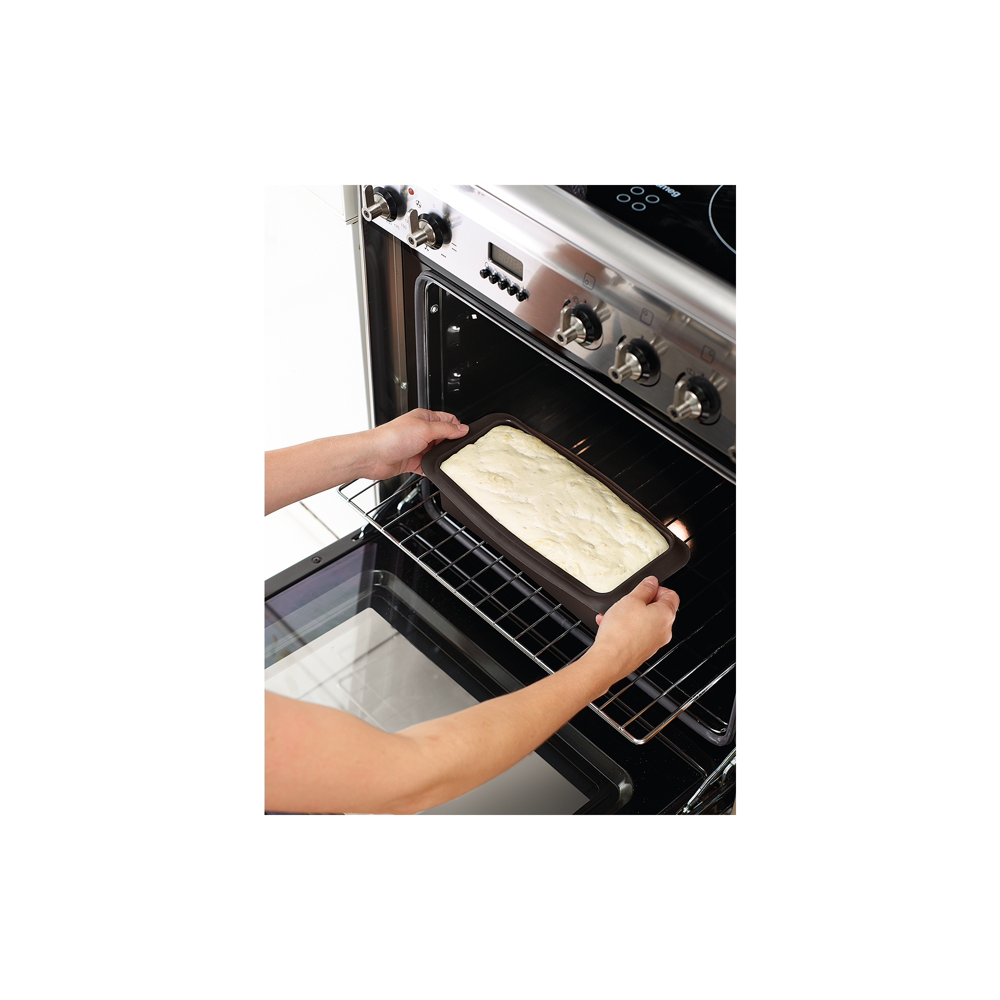 Person sliding a loaf pan with light dough into an open oven.