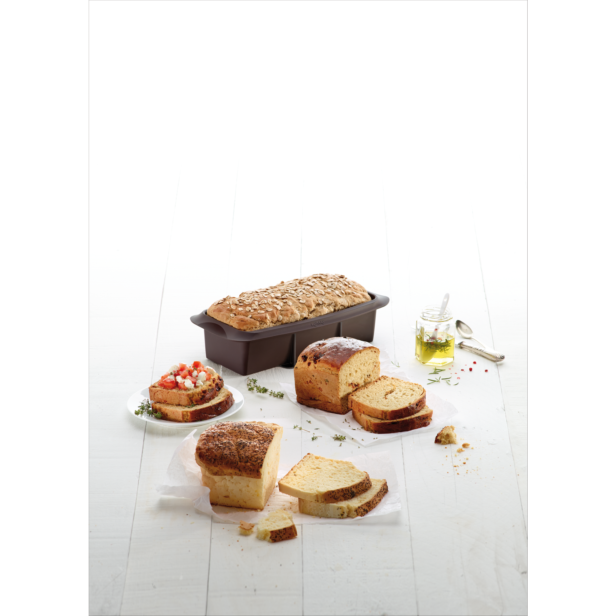 Freshly baked bread in silicone molds, sliced on a white wooden table with herbs and oil.