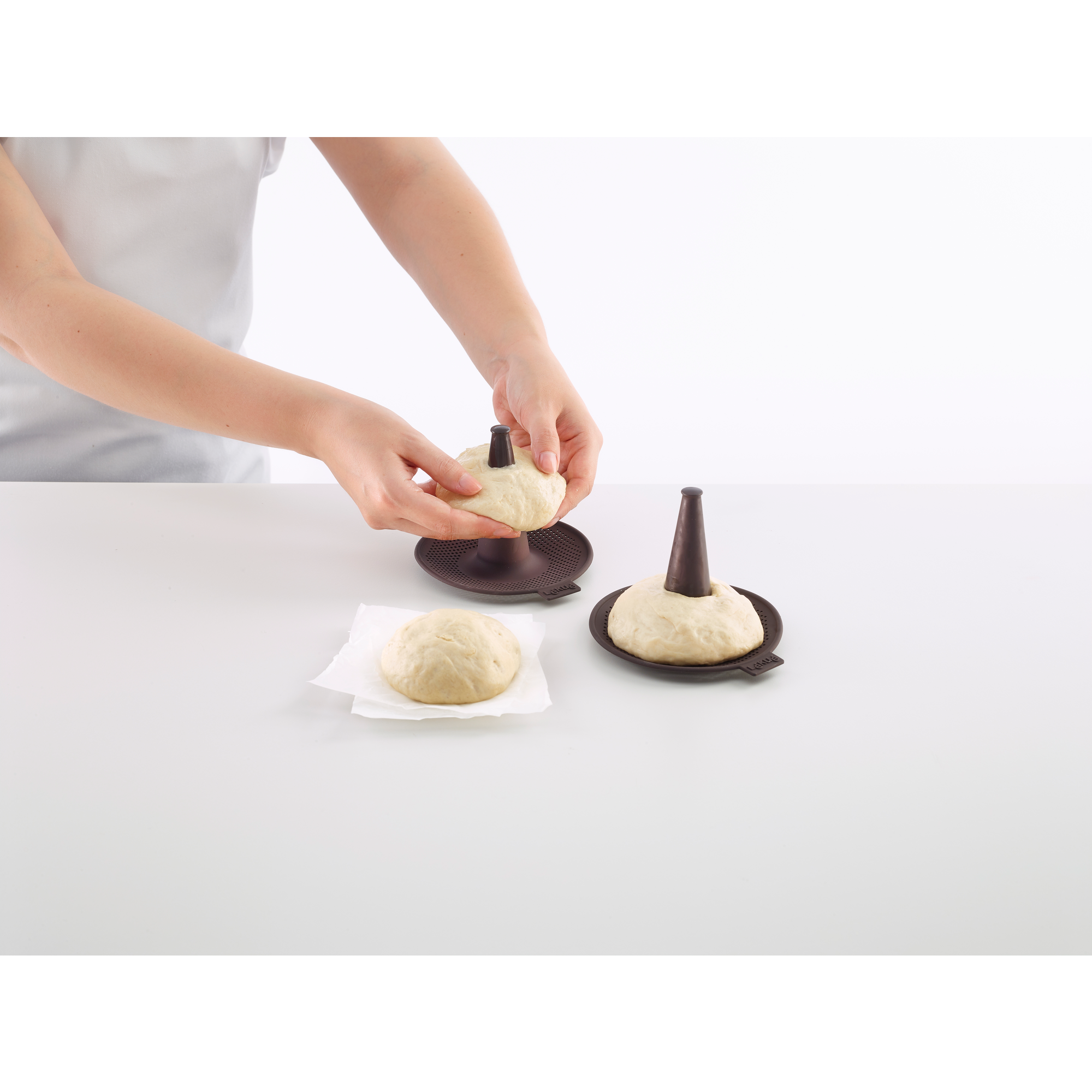 Person places dough onto a brown mold on a white table.