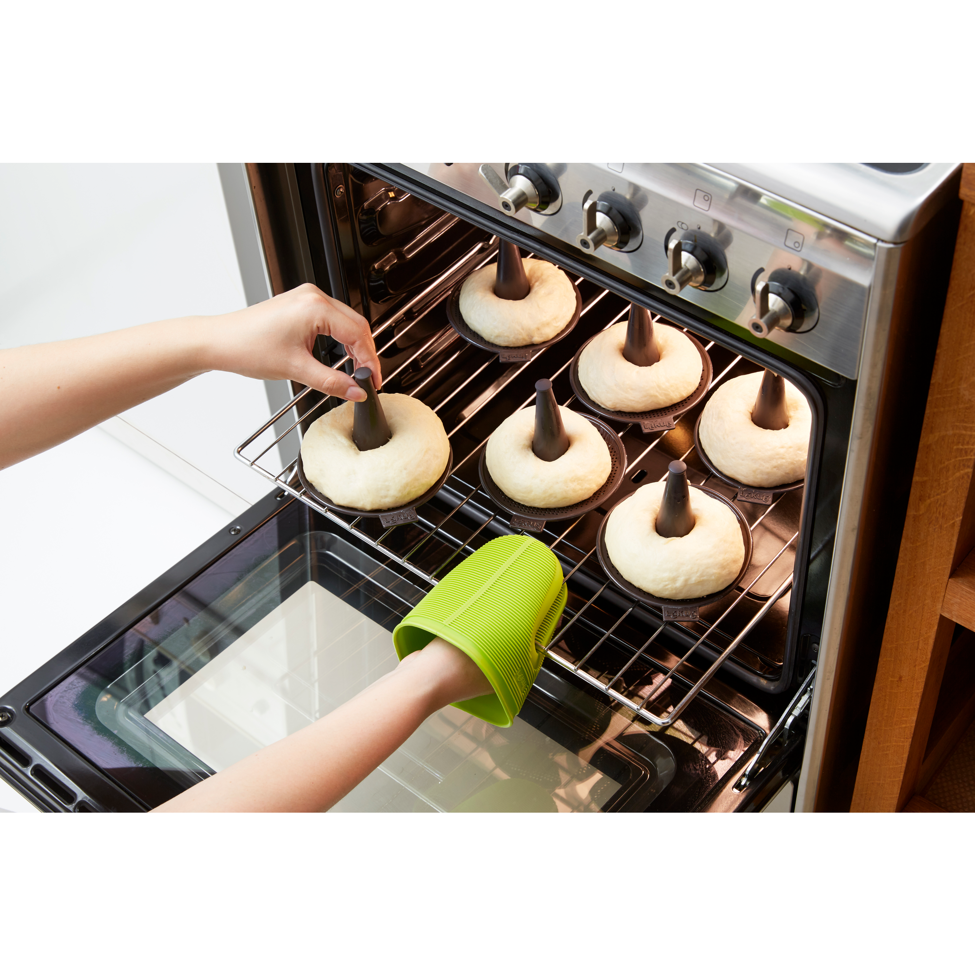 Someone places dough rings in molds on an oven rack inside an oven.