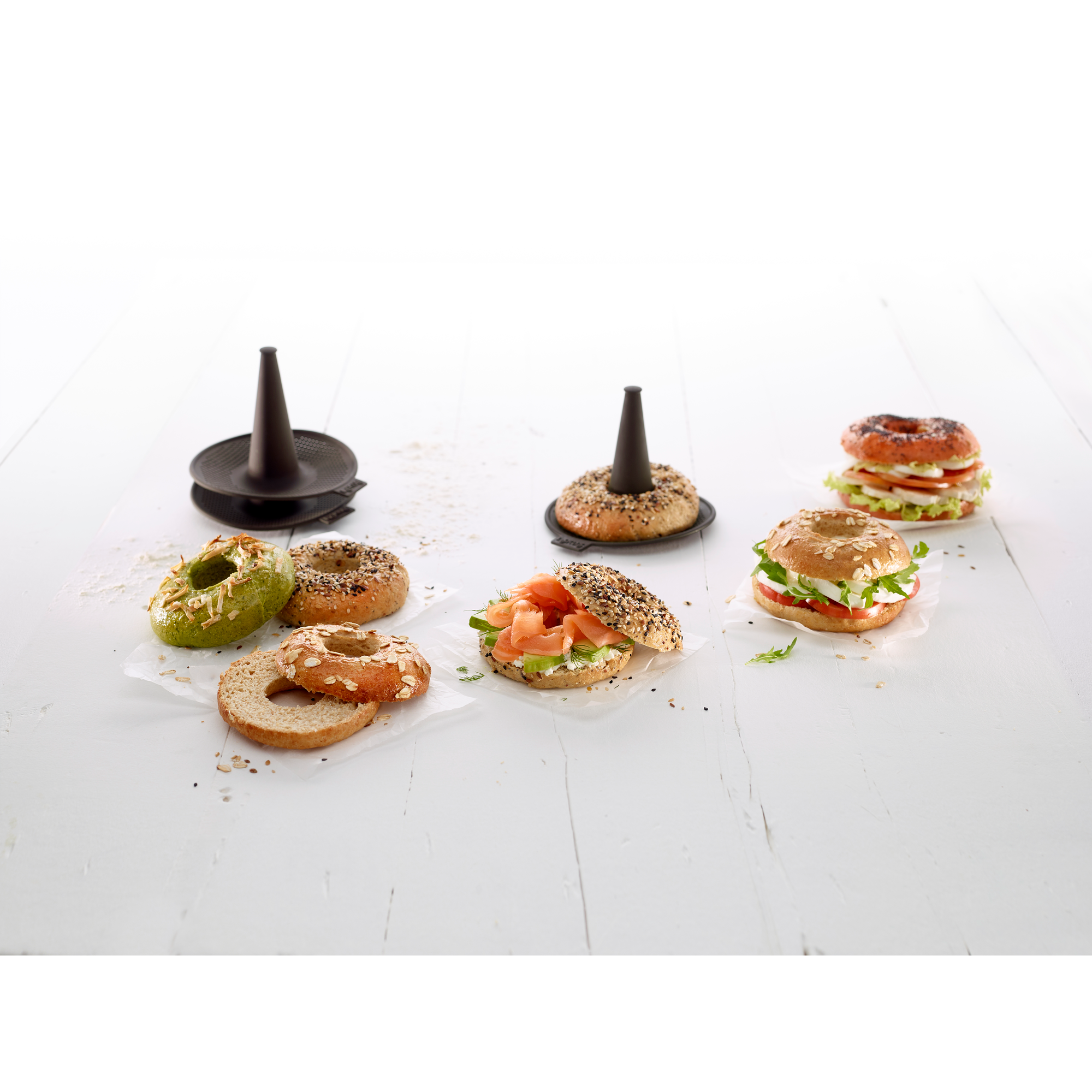 Various bagels, salmon and tomato-mozzarella sandwiches on a white wooden table with black baking molds.