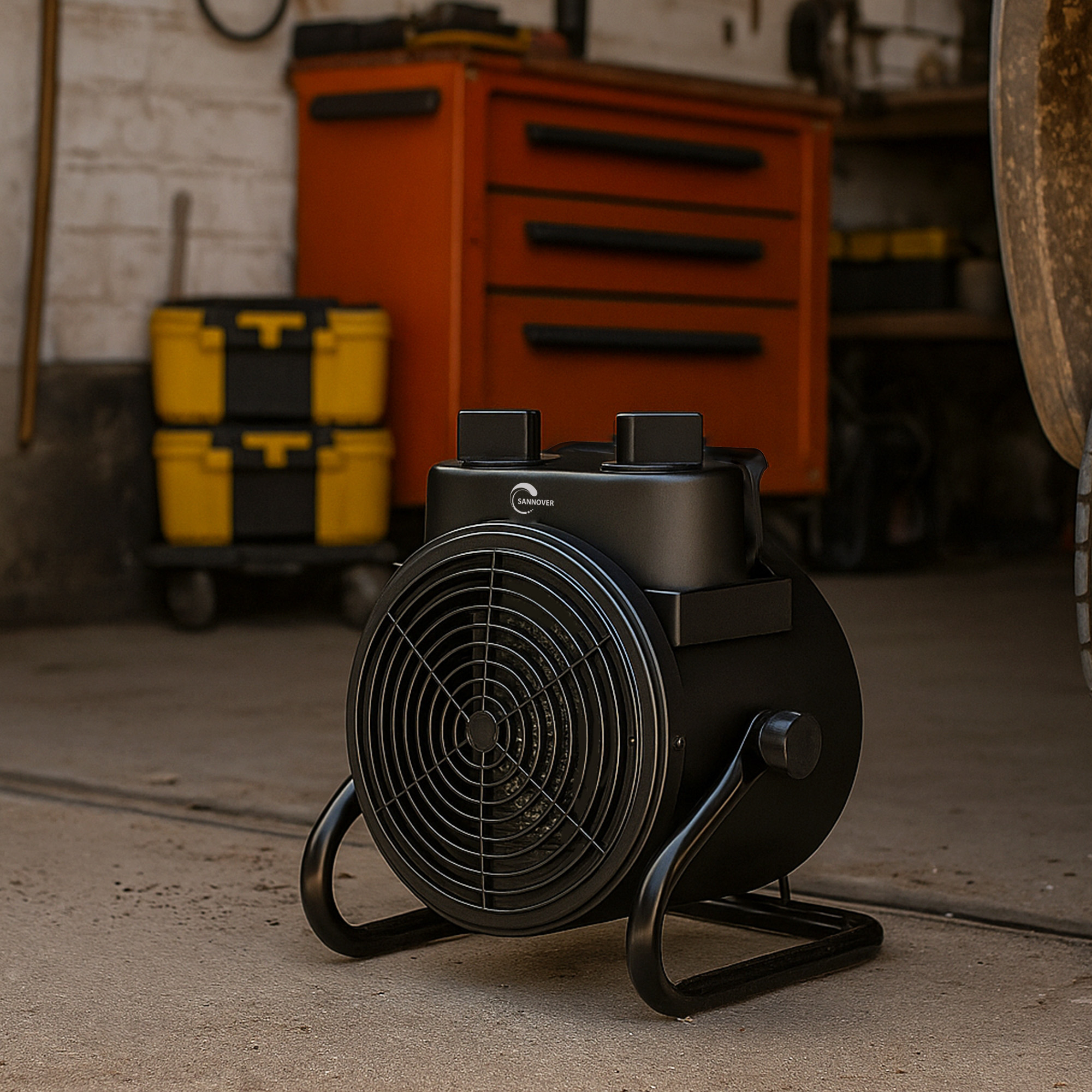 Un termoventilatore industriale nero su pavimento in cemento in un'officina con cassette degli attrezzi arancioni.