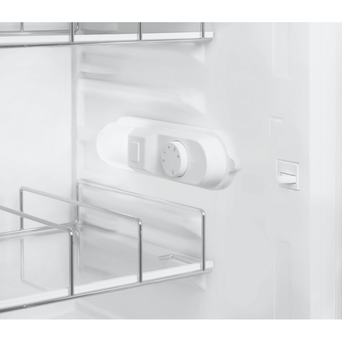 Vista interior de un refrigerador blanco con un selector de temperatura redondo, luz y estantes de alambre.