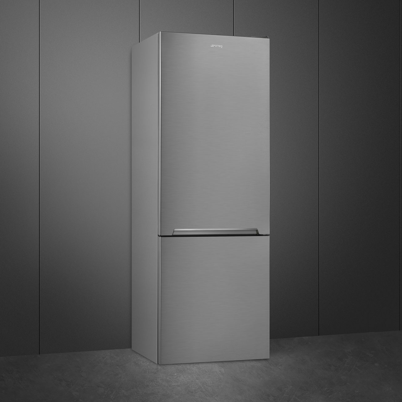 Un refrigerador Smeg plateado se encuentra sobre un piso oscuro contra una pared gris.