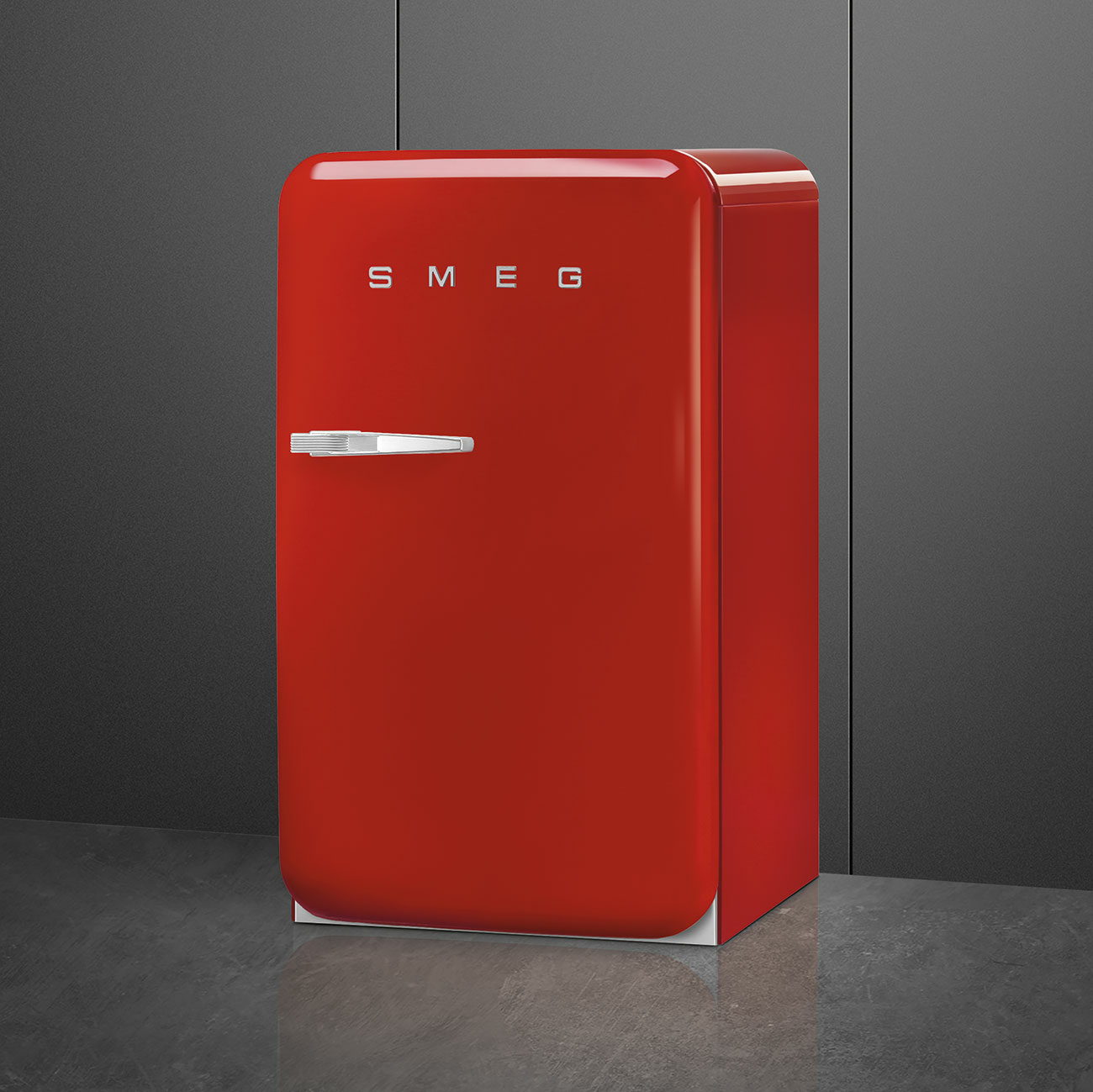 Un refrigerador Smeg rojo brillante se encuentra en una encimera gris contra una pared oscura.
