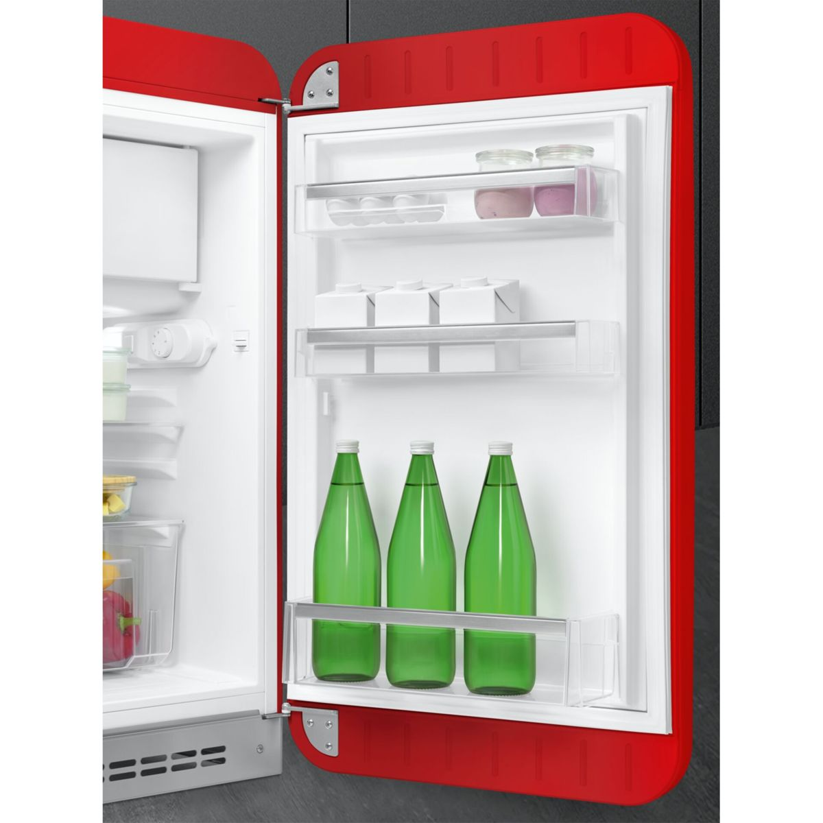 Frigorífico retro rojo abierto con estantes organizados que contienen botellas verdes, cartones y tarros.