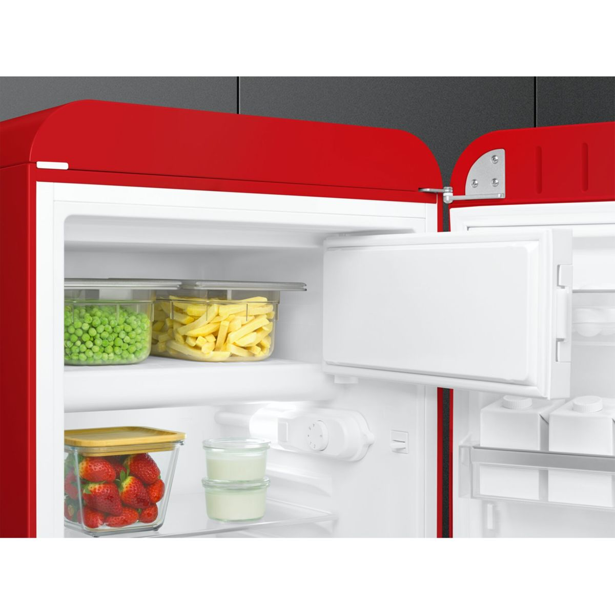 Una nevera roja abierta con estantes que contienen recipientes con guisantes, patatas fritas, fresas y yogur.