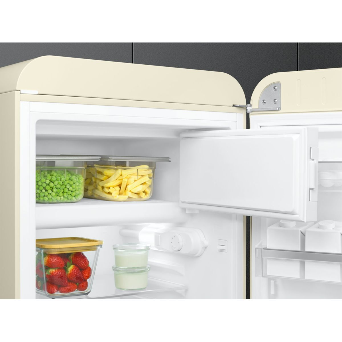 Frigorífico beige abierto lleno de guisantes, patatas fritas y fresas frescas en recipientes.