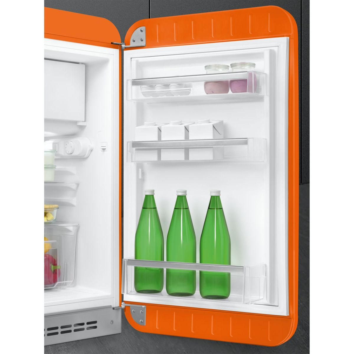 Una puerta de refrigerador retro naranja abierta con comida, frascos y tres botellas verdes.
