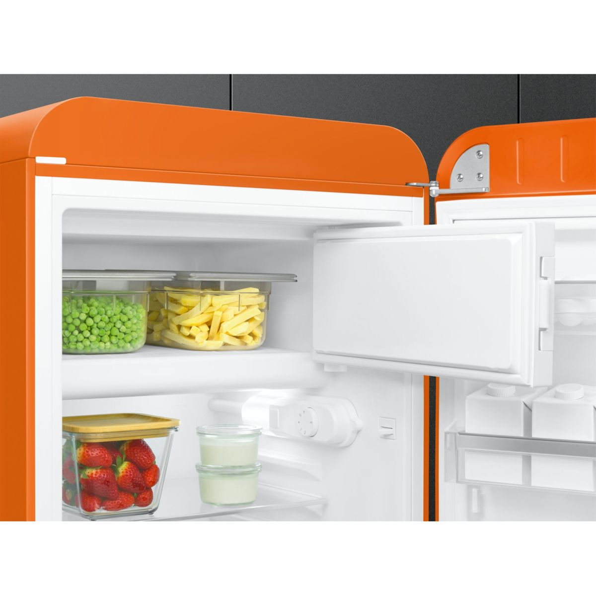 Un refrigerador retro naranja abierto lleno de recipientes con guisantes, patatas fritas, fresas y yogur.