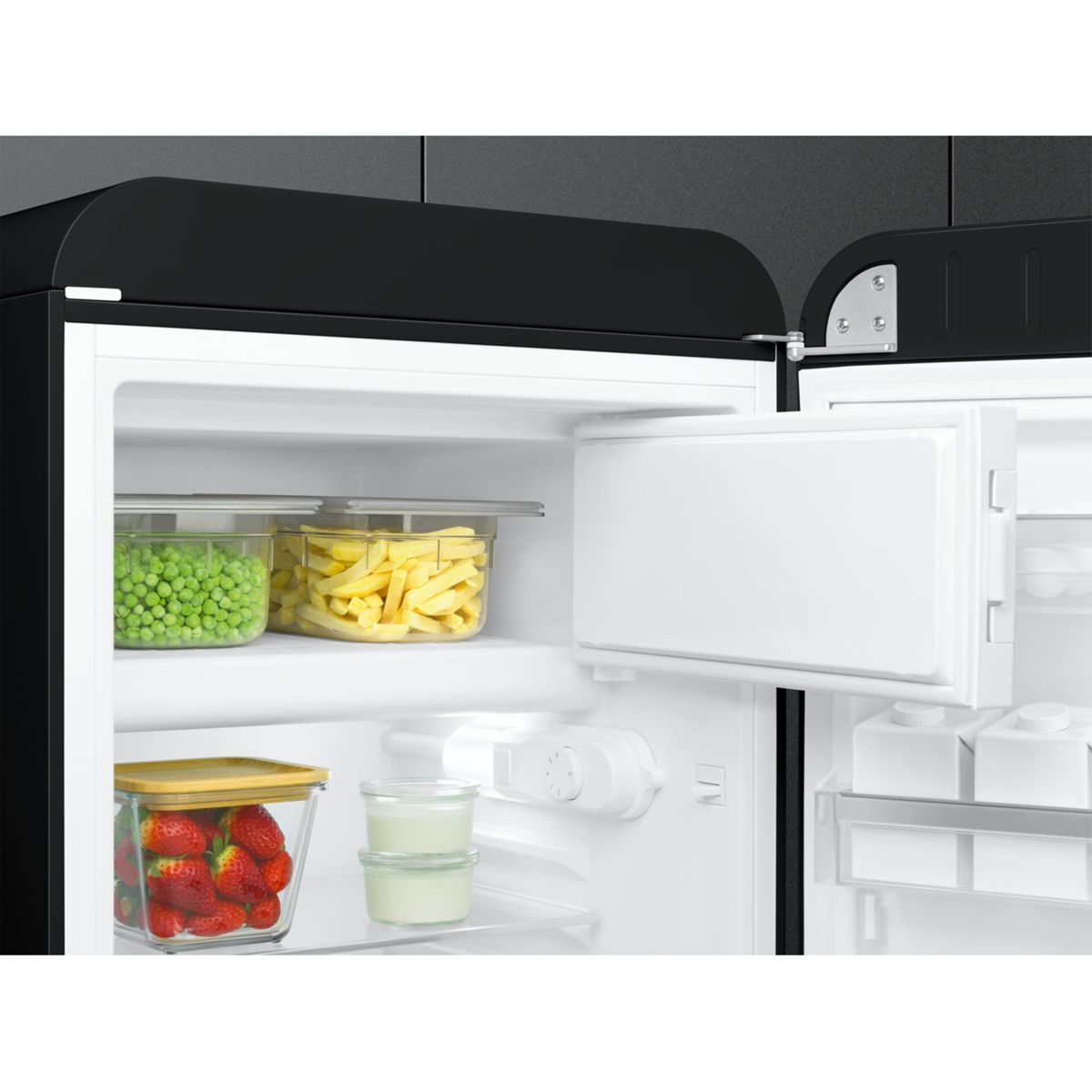 Vista interior de un refrigerador negro abierto con recipientes de comida, guisantes, patatas, fresas y yogur.