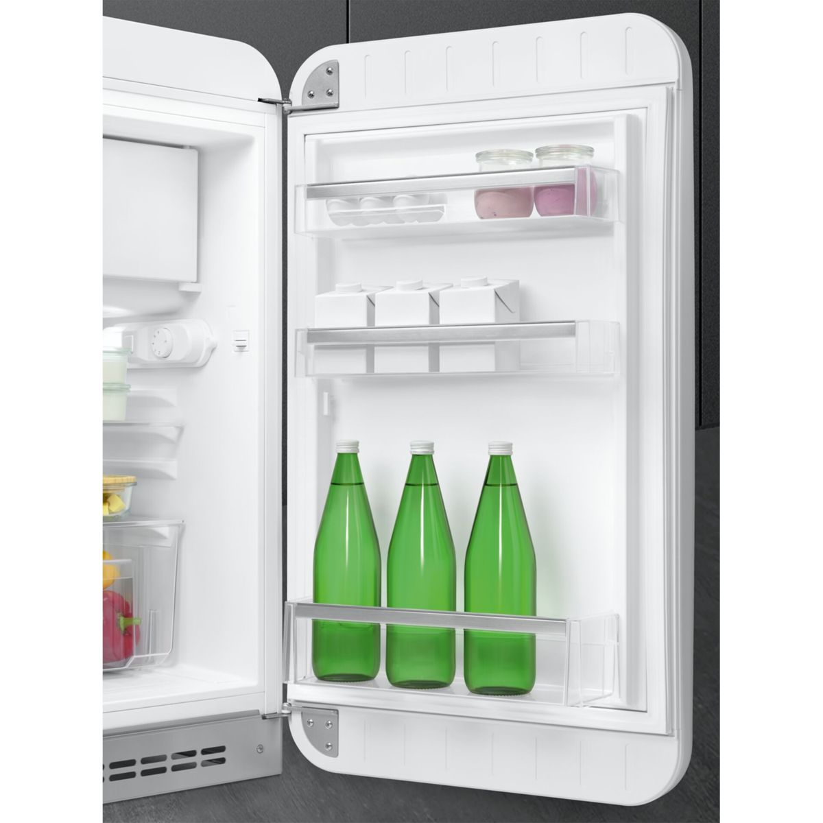 Puerta de refrigerador blanca abierta con tres estantes que contienen tarros, cartones y tres botellas verdes.