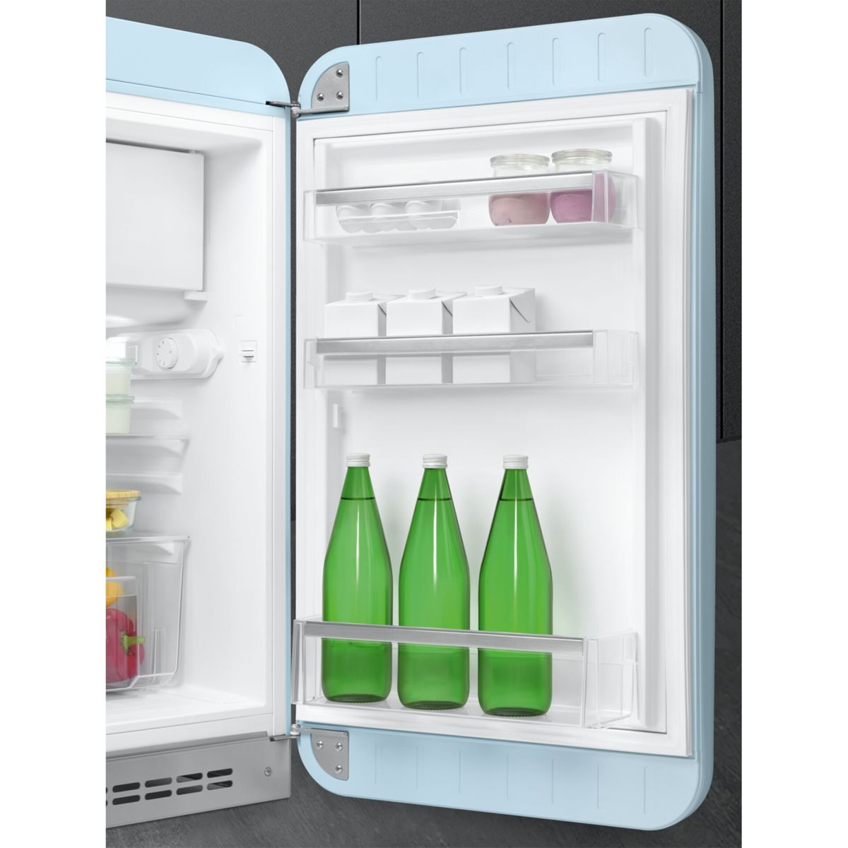 Frigorífico azul claro abierto con alimentos, cartones de leche y botellas verdes en las baldas.