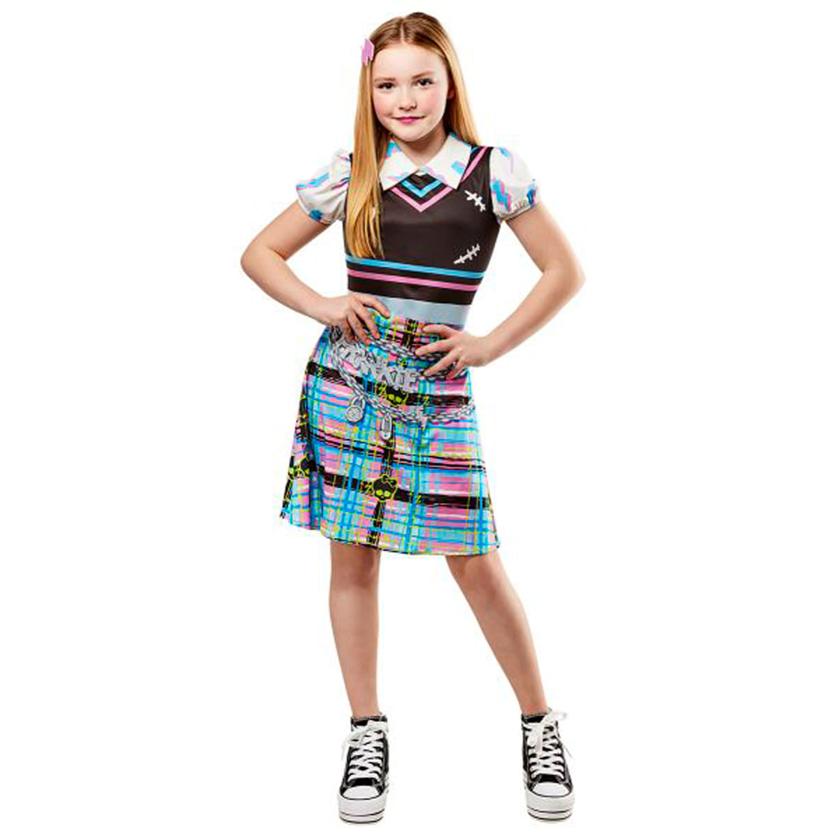 Una niña rubia con un colorido vestido de Monster High y zapatillas negras posa contra un fondo blanco.