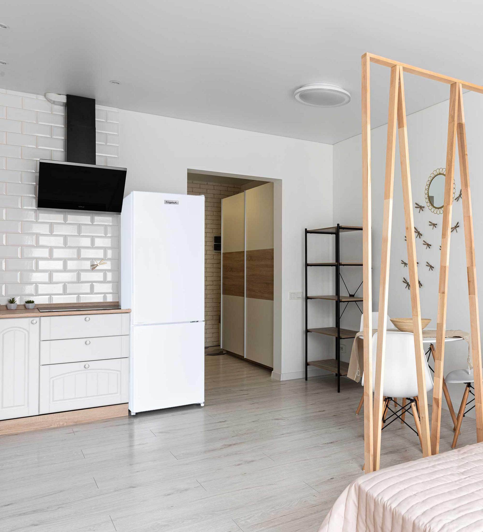 Una cocina moderna con nevera blanca, ladrillo blanco, campana negra y comedor tras un separador de madera.