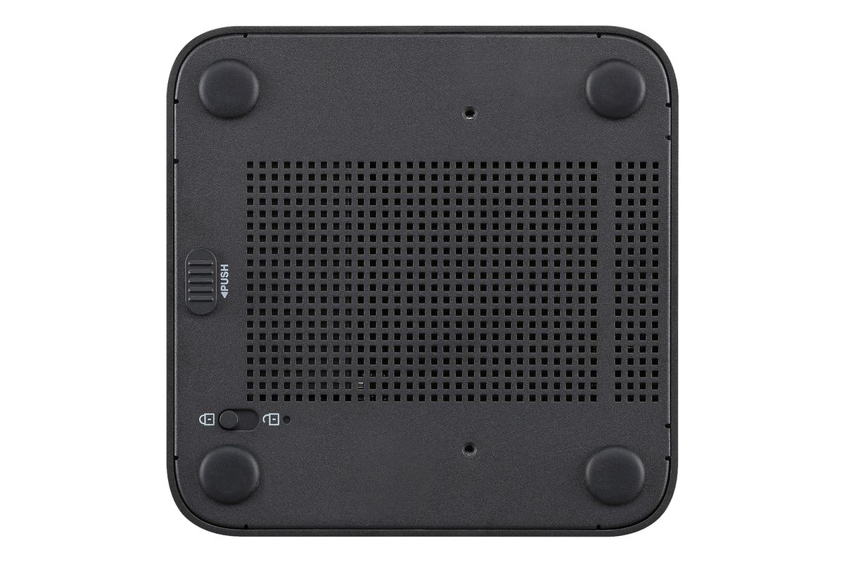 Parte inferior de un dispositivo electrónico negro con cuatro patas de goma, rejilla de ventilación y bloqueo.
