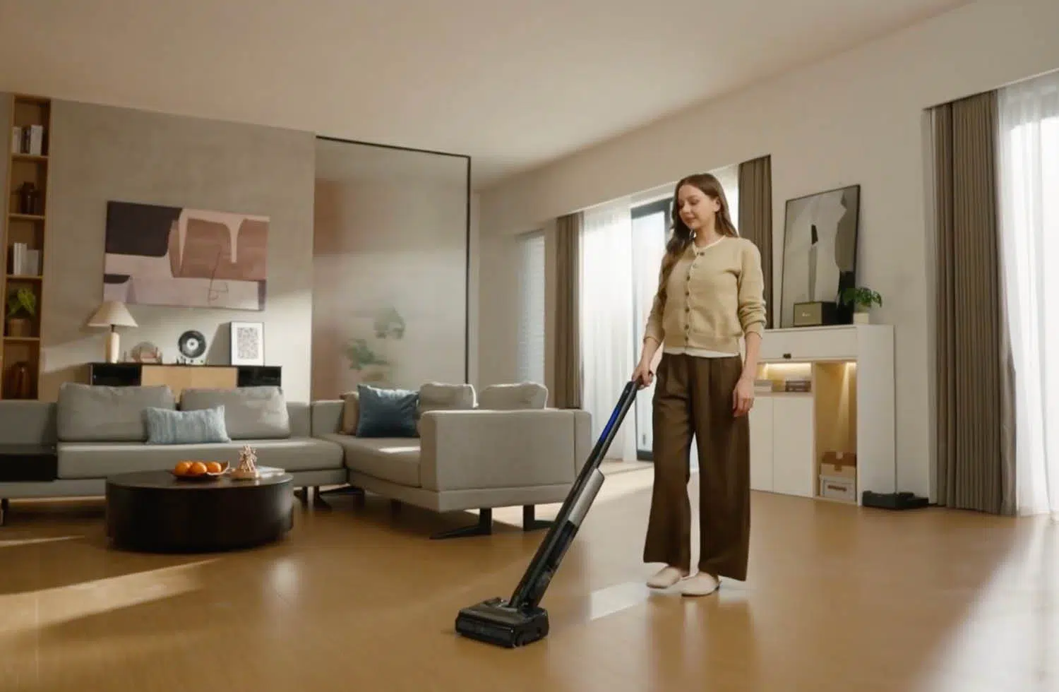 Una mujer aspira un suelo de madera en una sala de estar moderna con un sofá gris.
