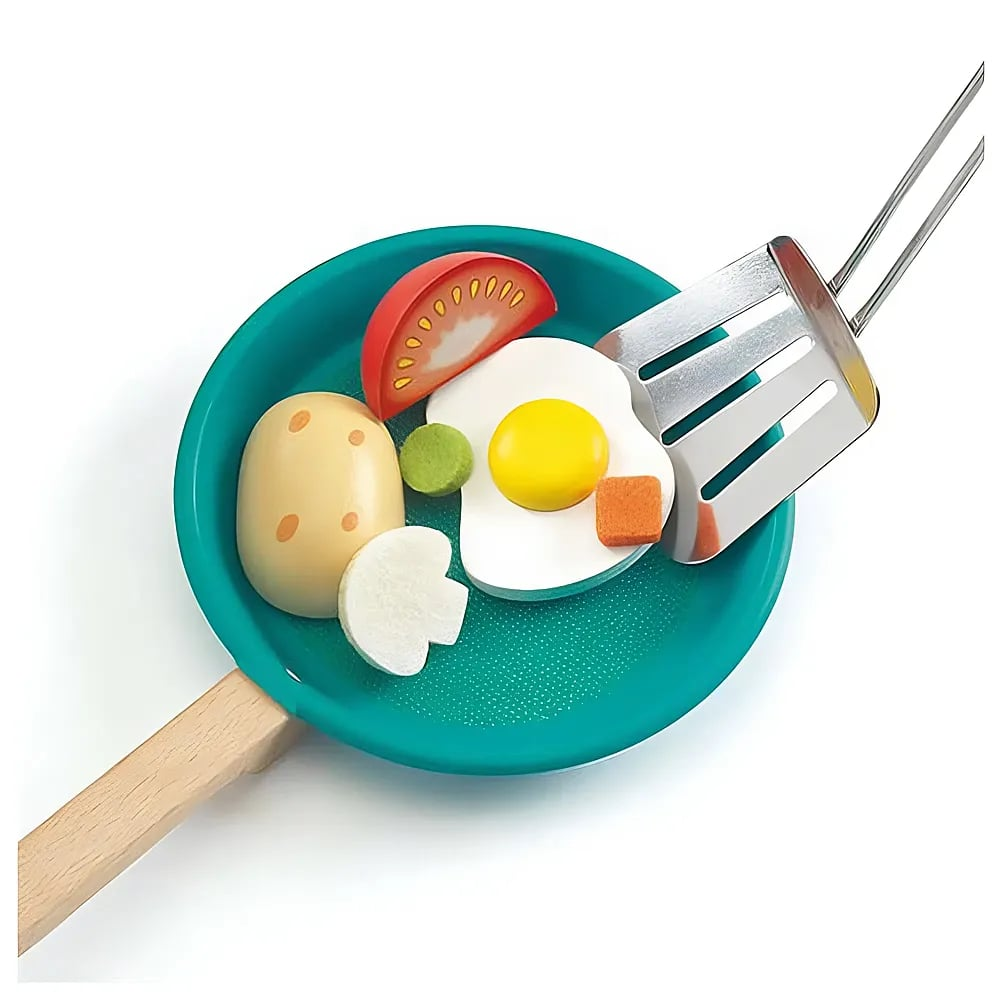 Eine grüne Spielzeug-Pfanne mit Holzlöffel und hölzernem Ei, Tomate, Pilz und Kartoffel auf weißem Grund.