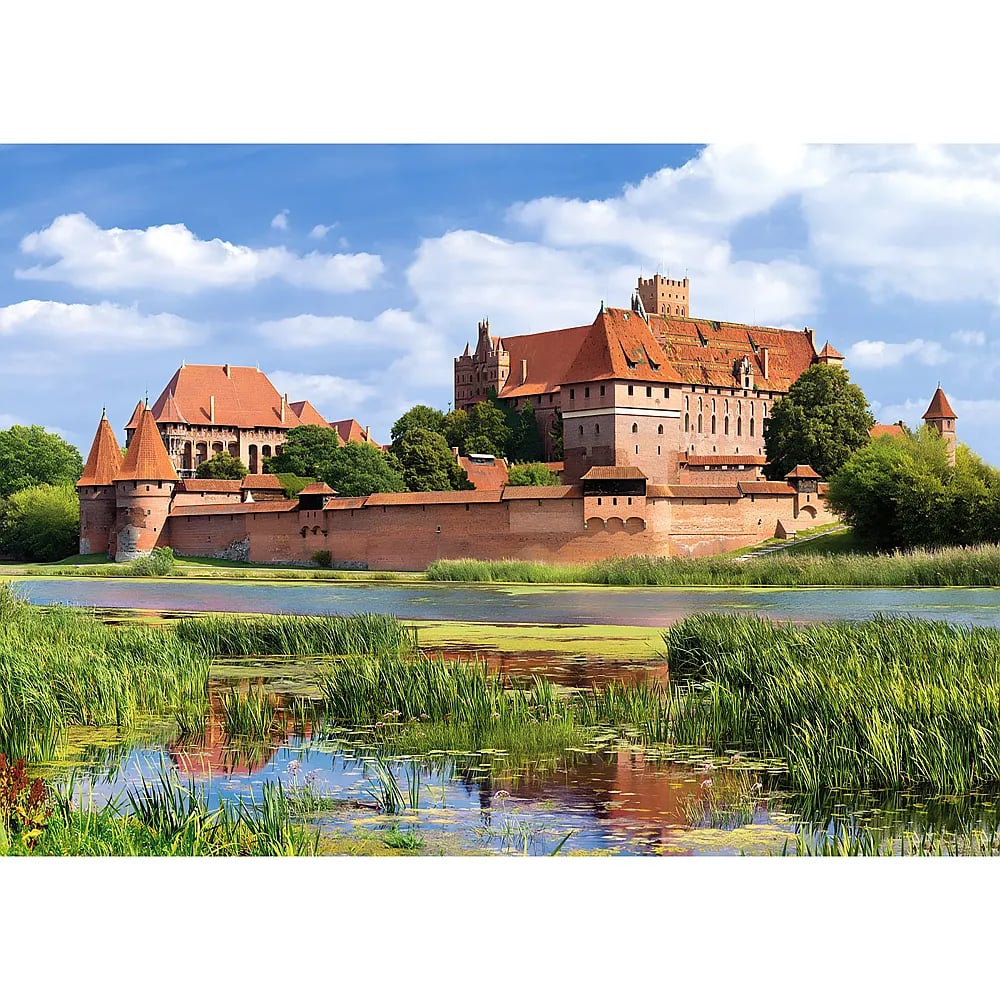 Eine große rote Backsteinburg steht an einem Fluss, umgeben von grünem Schilf unter blauem Himmel.