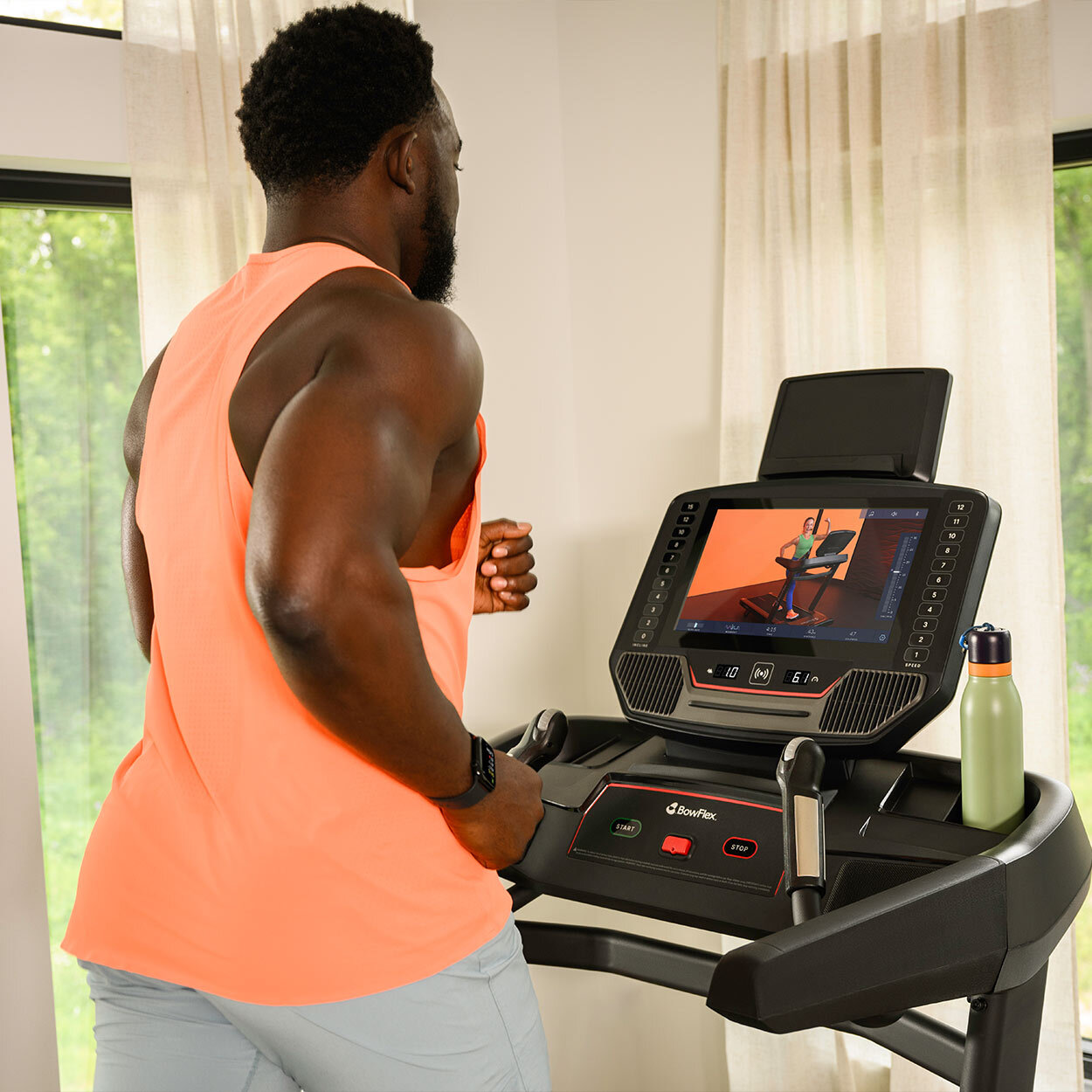 Ein schwarzer Mann in einem orangen Tanktop läuft auf einem Laufband und schaut auf den Bildschirm.