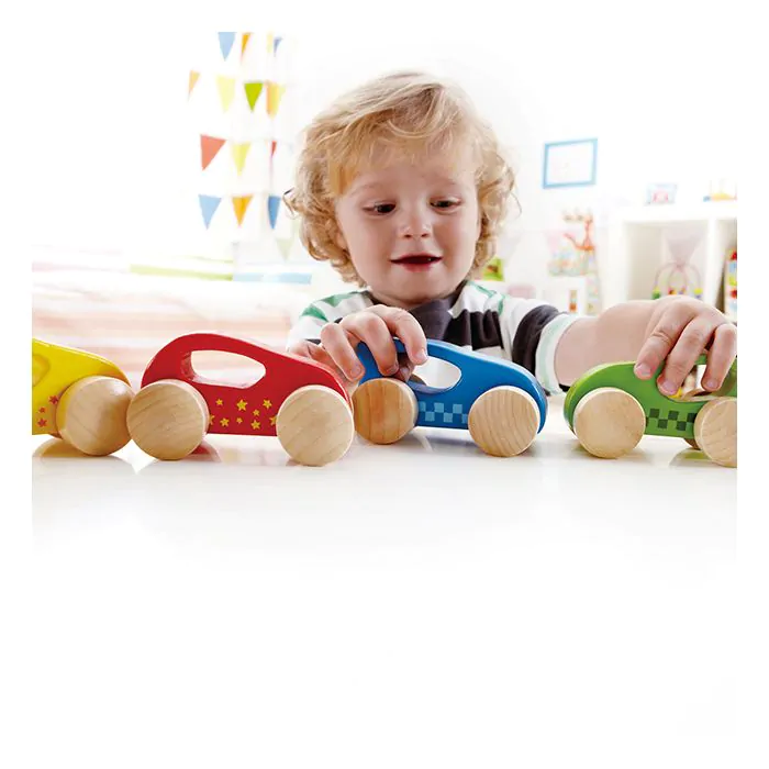 Niño pequeño jugando con cuatro autos de juguete de madera coloridos.