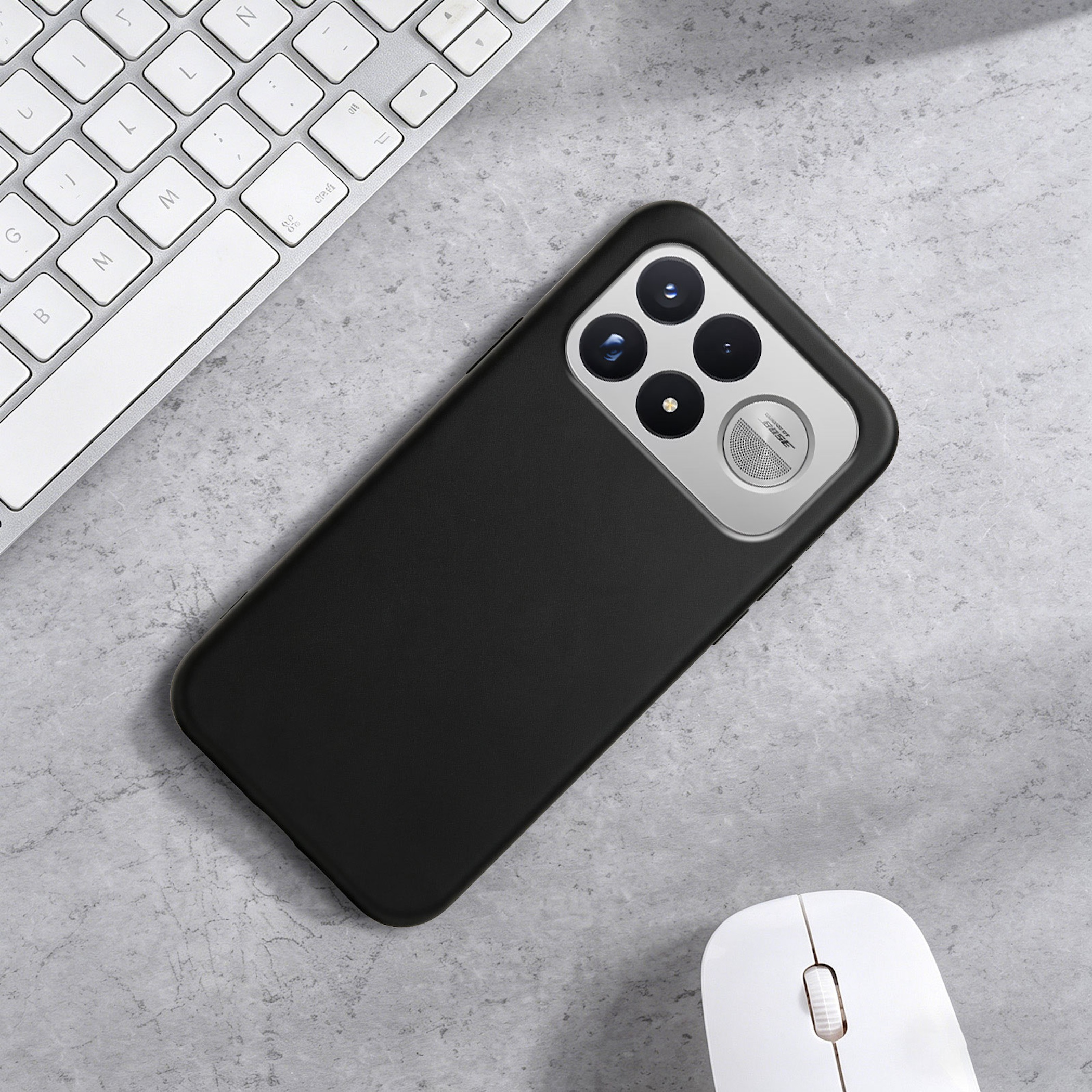 Ein schwarzes Smartphone mit Vierfachkamera liegt auf einem grauen Tisch neben einer Tastatur und einer Maus.