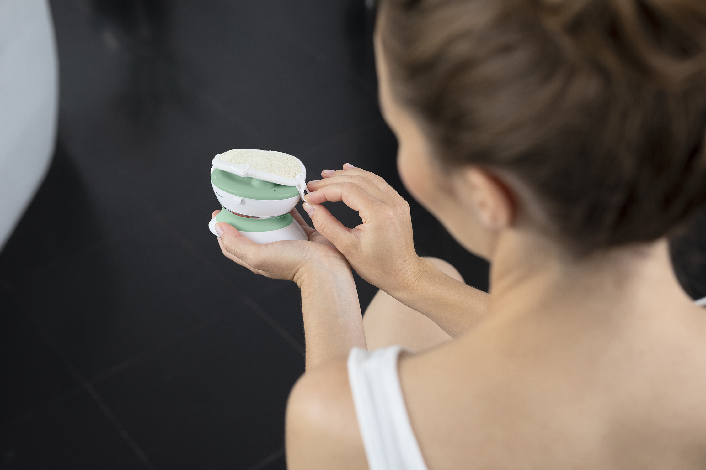 A woman holds a white and green exfoliating device in her hands.