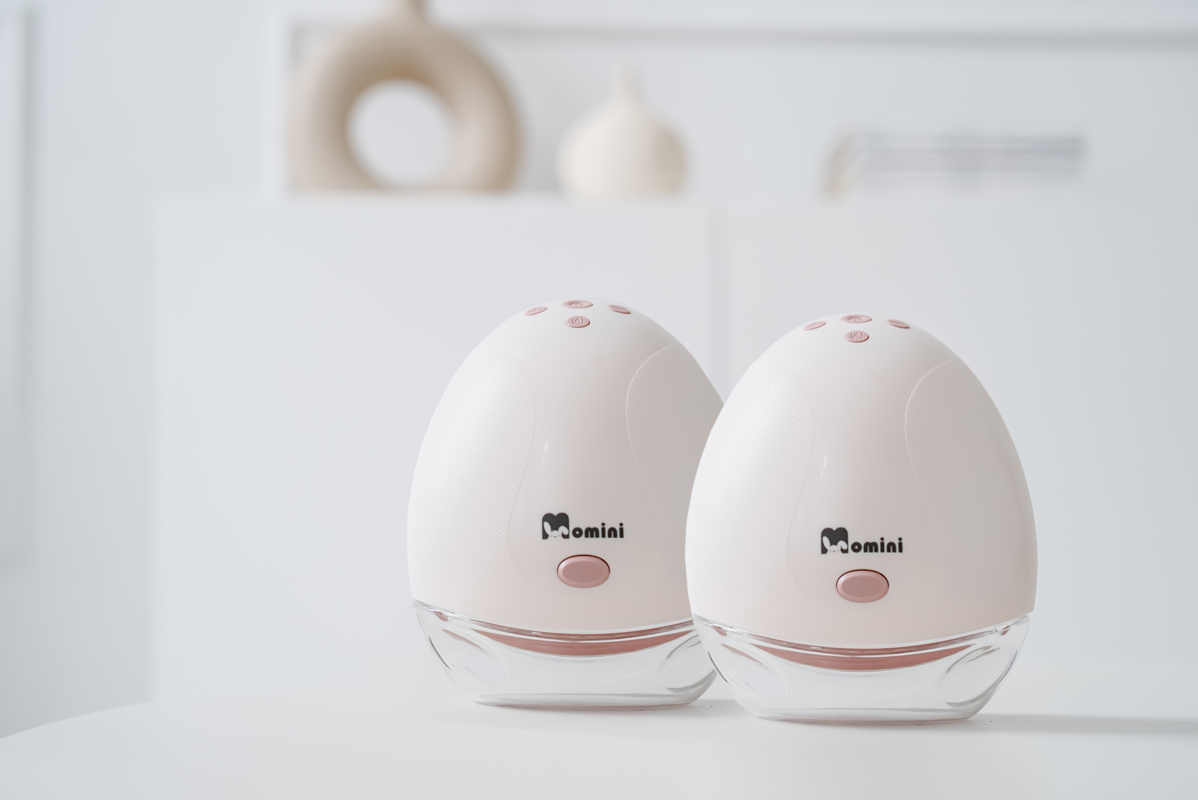 Due tiralatte elettrici Momini bianchi e rosa sono affiancati su una superficie bianca.