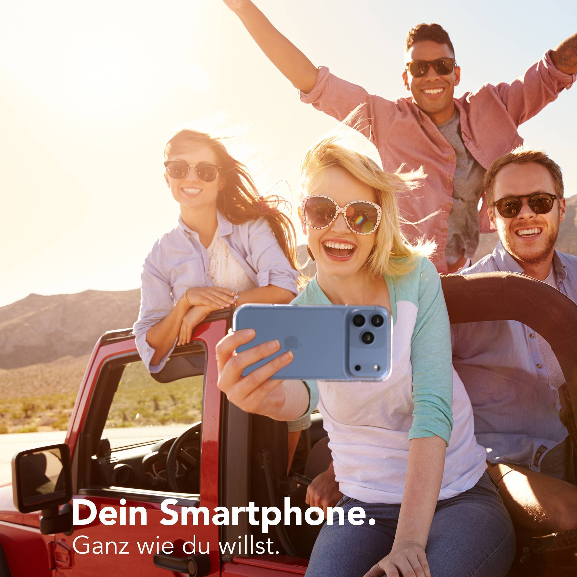 Vier glückliche Freunde machen ein Selfie in einem roten Geländewagen unter strahlender Sonne.
