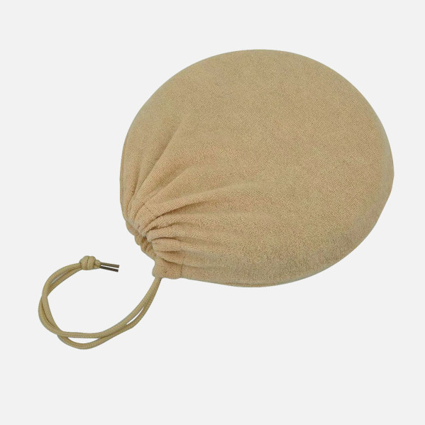 Una bolsa de almacenamiento de tela redonda beis con cordón sobre fondo gris claro.
