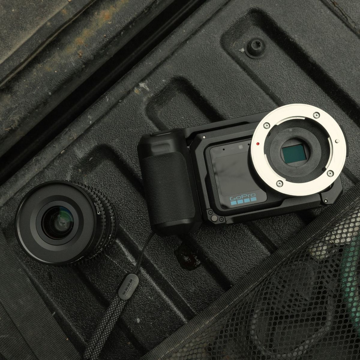 Una cámara GoPro con montura y un objetivo separado descansan sobre la superficie oscura y texturizada de un camión.