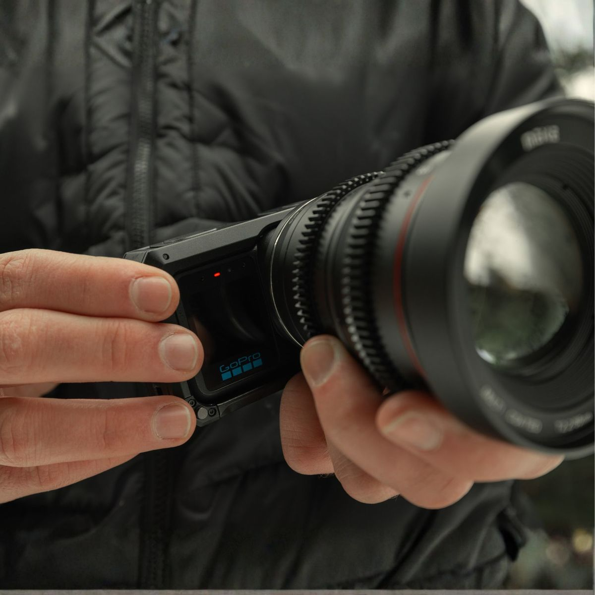 Una persona con chaqueta negra sostiene una cámara GoPro compacta con gran lente de cine.