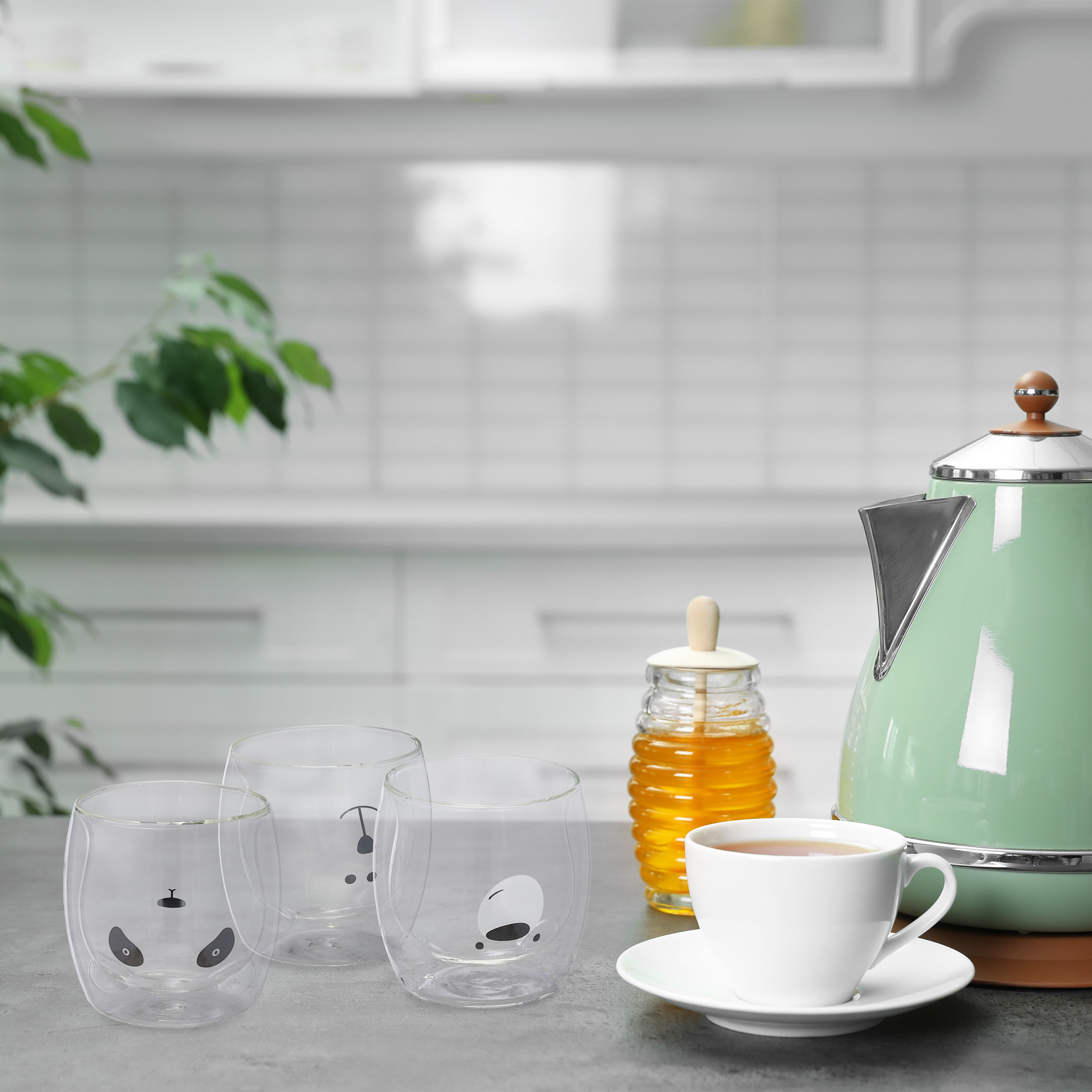 Gläser, Honigtopf, Teetasse mit Untertasse und ein mintgrüner Wasserkocher stehen auf einer Arbeitsplatte in der Küche.