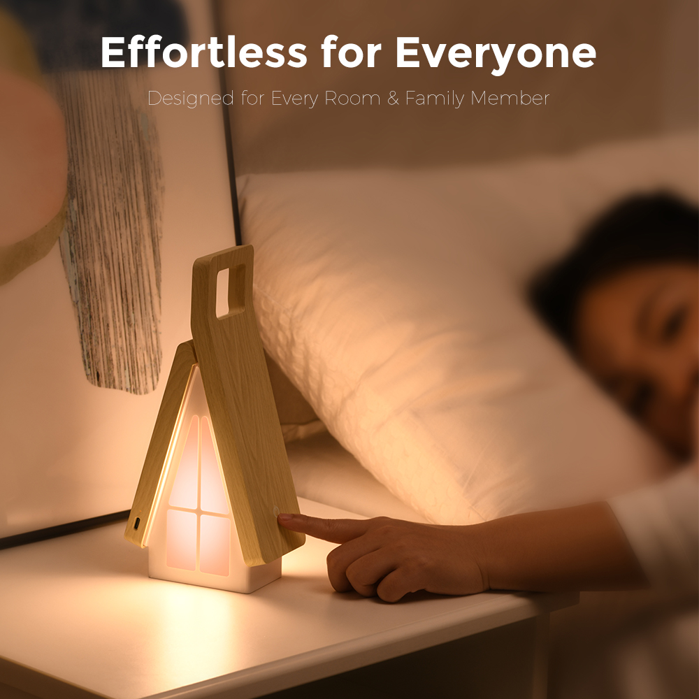 Eine Hand schaltet eine hölzerne, hausförmige Nachtlampe auf einem Nachttisch ein.