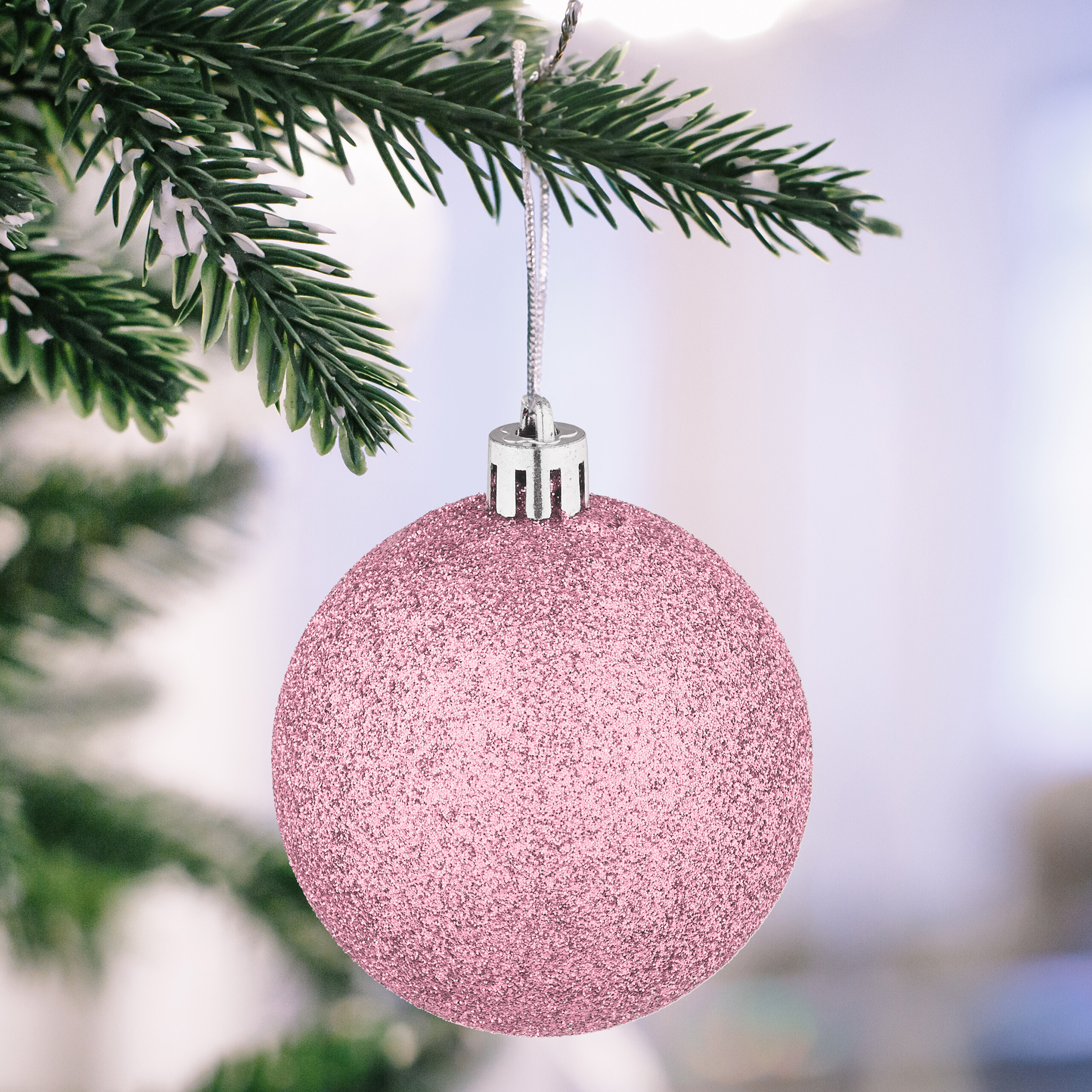 Eine glitzernde rosa Weihnachtskugel hängt an einem schneebedeckten Tannenast.
