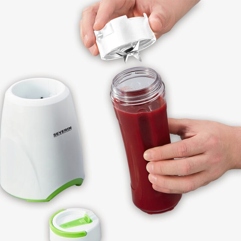 Las manos enroscan el accesorio de cuchilla en una botella de batido roja junto a la licuadora blanca.