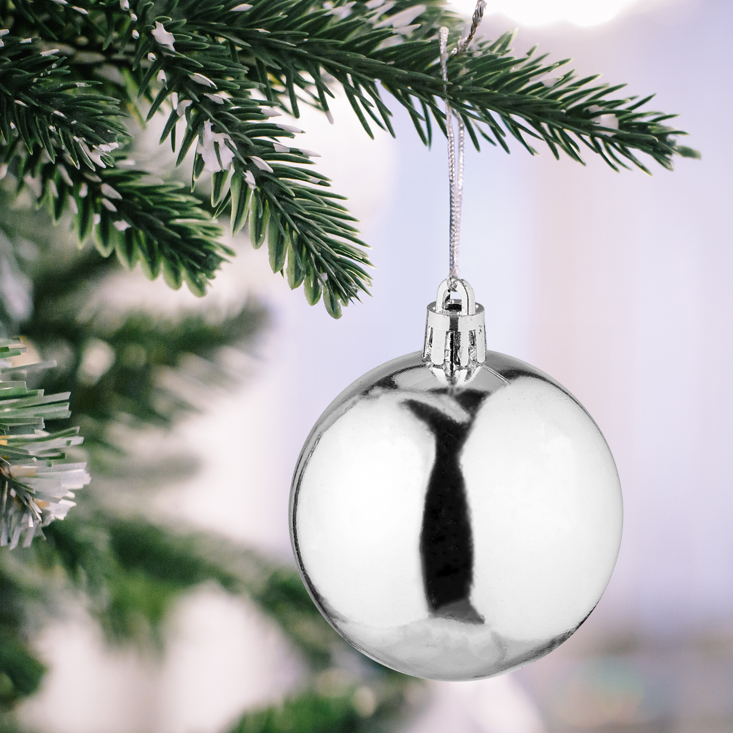 Eine glänzende Silberkugel hängt an einem Weihnachtsbaum mit grünen Zweigen.