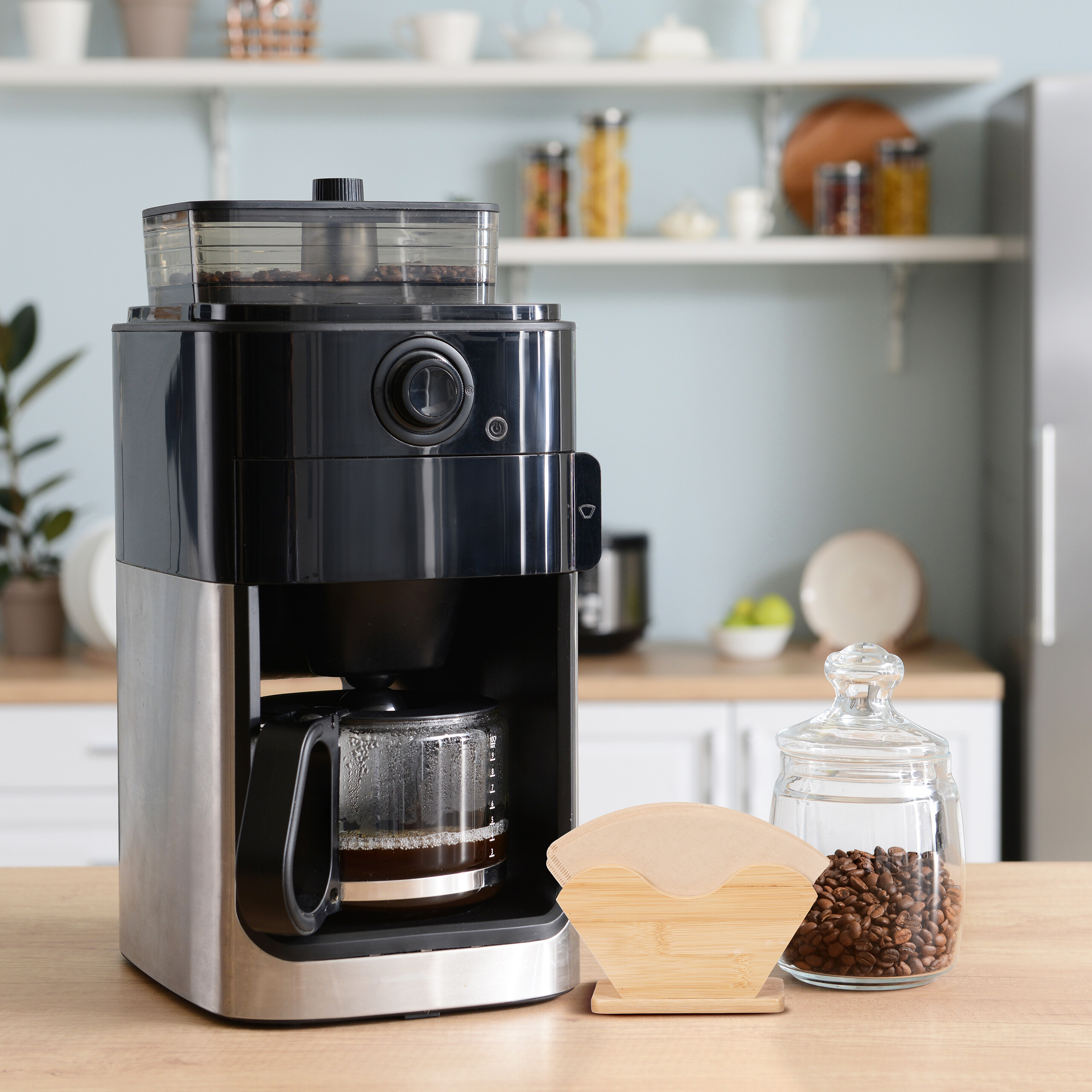 Moderne schwarze und silberne Filterkaffeemaschine auf einer Küchentheke mit Kaffeebohnen.