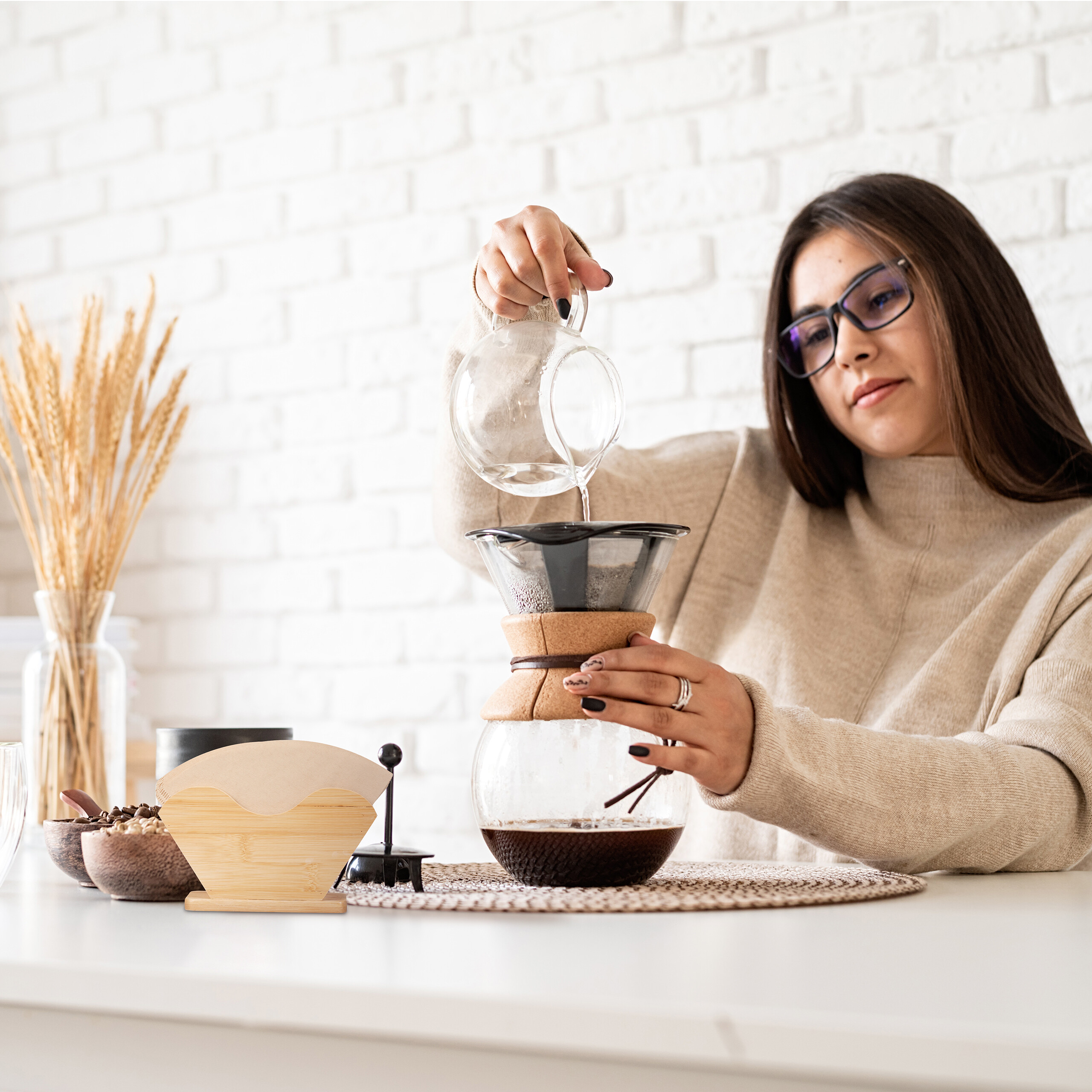Eine Frau gießt Wasser aus einem Glaskessel in einen Kaffeebereiter auf einem Tisch.