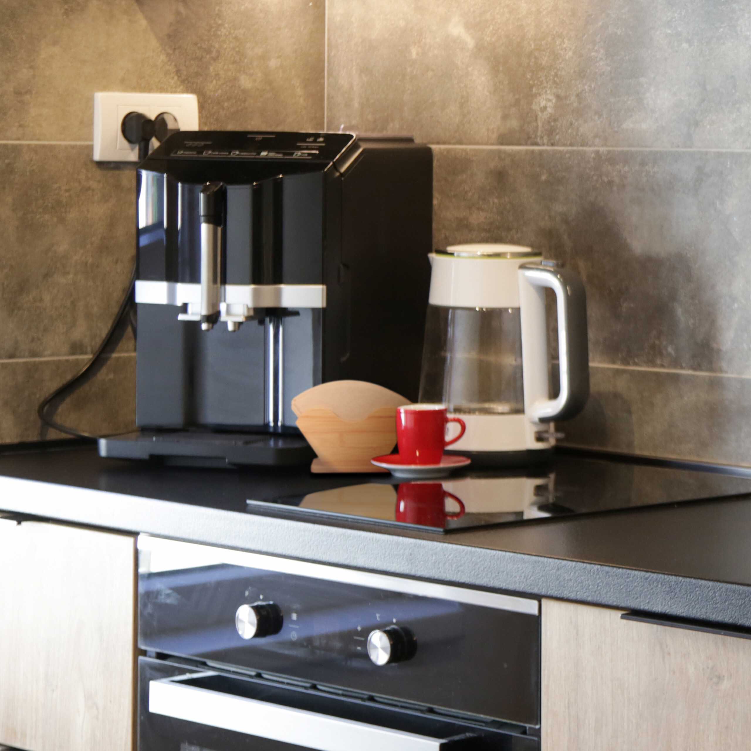 Schwarze Kaffeemaschine, weißer Wasserkocher und eine rote Tasse auf der Arbeitsplatte in der Küche.