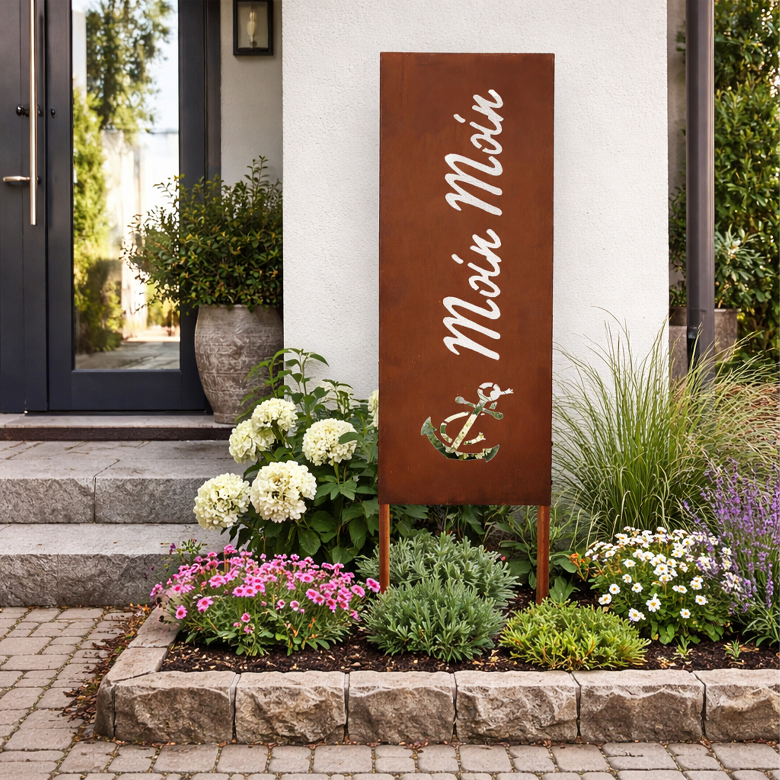 Rostfarbene Gartensäule mit Aufschrift 'Moin Moin' und Anker, umgeben von Blumen und Pflanzen.