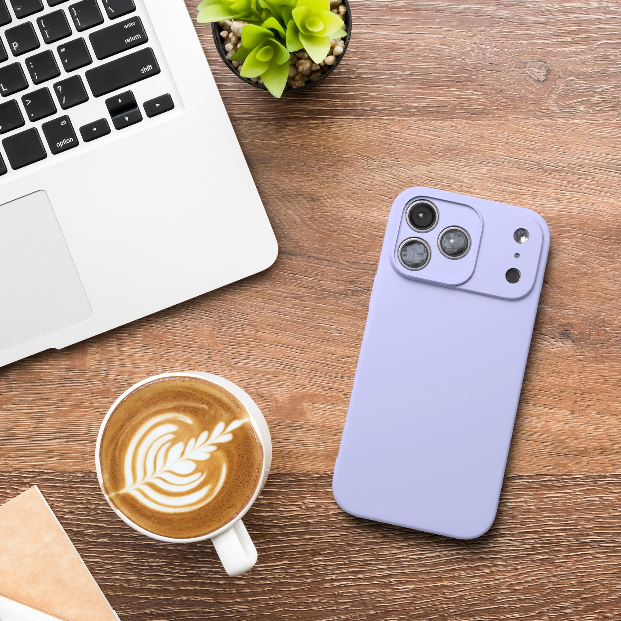 Lila Handy, Kaffeetasse mit Latte Art, Laptop und kleine Pflanze auf Holztisch.
