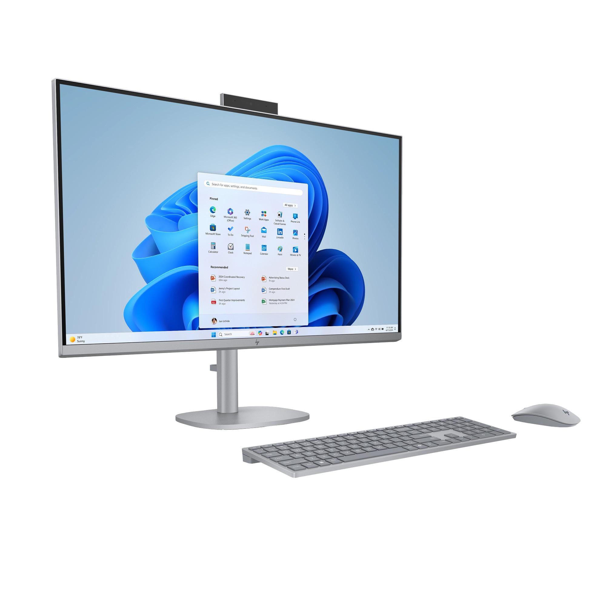 Una computadora todo en uno plateada con teclado y ratón, mostrando un escritorio de Windows sobre fondo blanco.