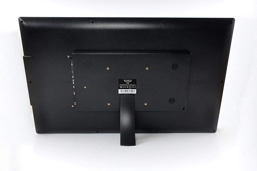Il retro di un monitor nero con supporto, porte e un'etichetta su un tavolo bianco.