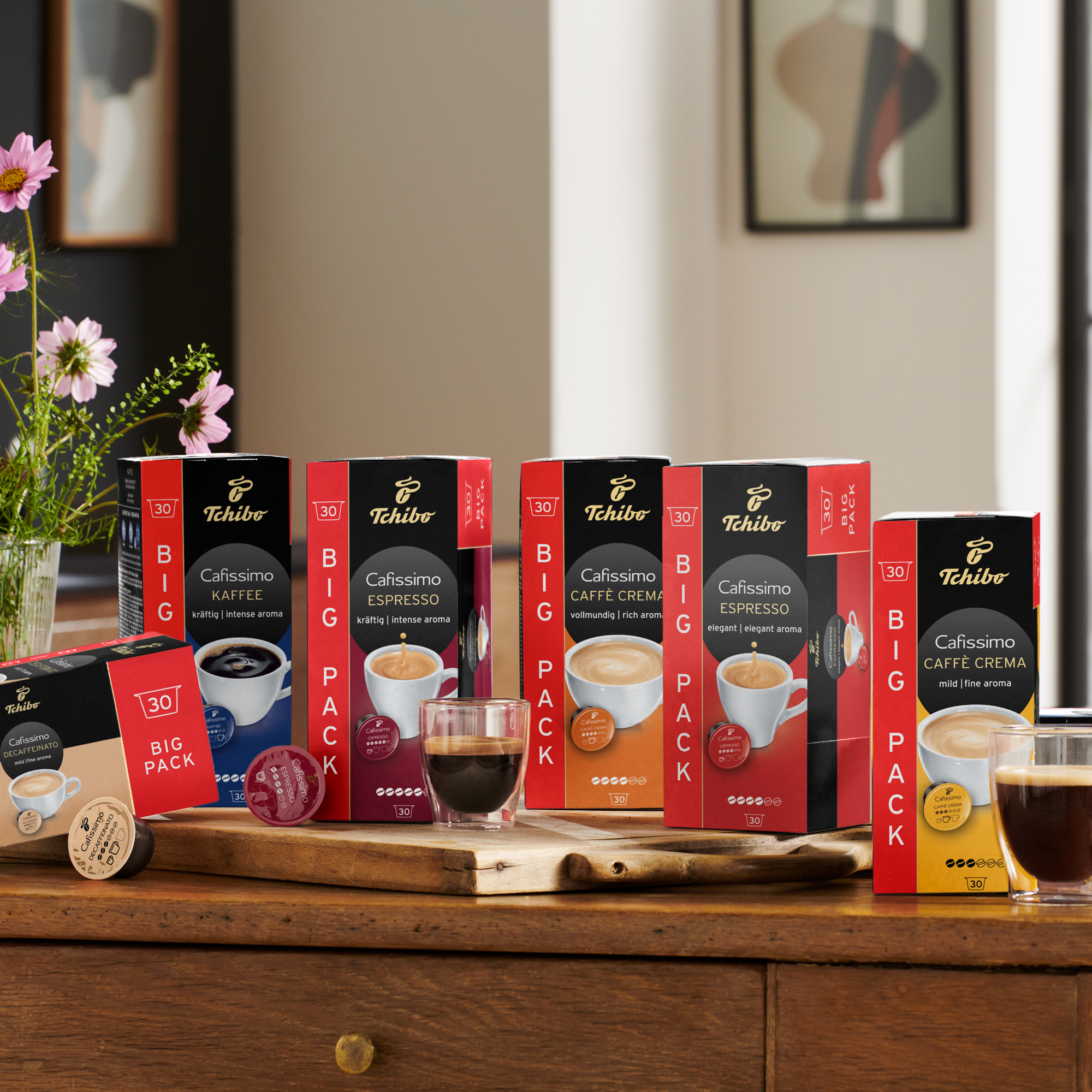 Verschiedene Tchibo Cafissimo Kaffeepackungen und Tassen auf einem Holzbrett.