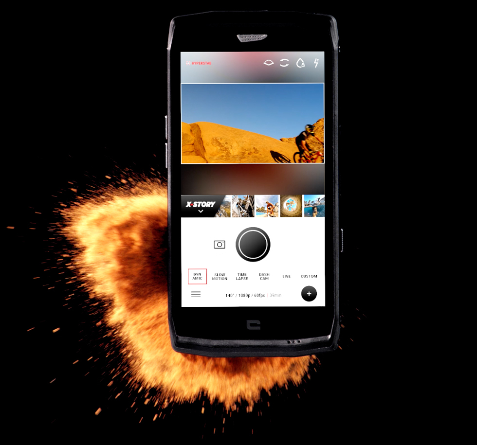 Un smartphone negro muestra una app de cámara en pantalla, rodeado por una explosión de fuego y chispas naranjas.