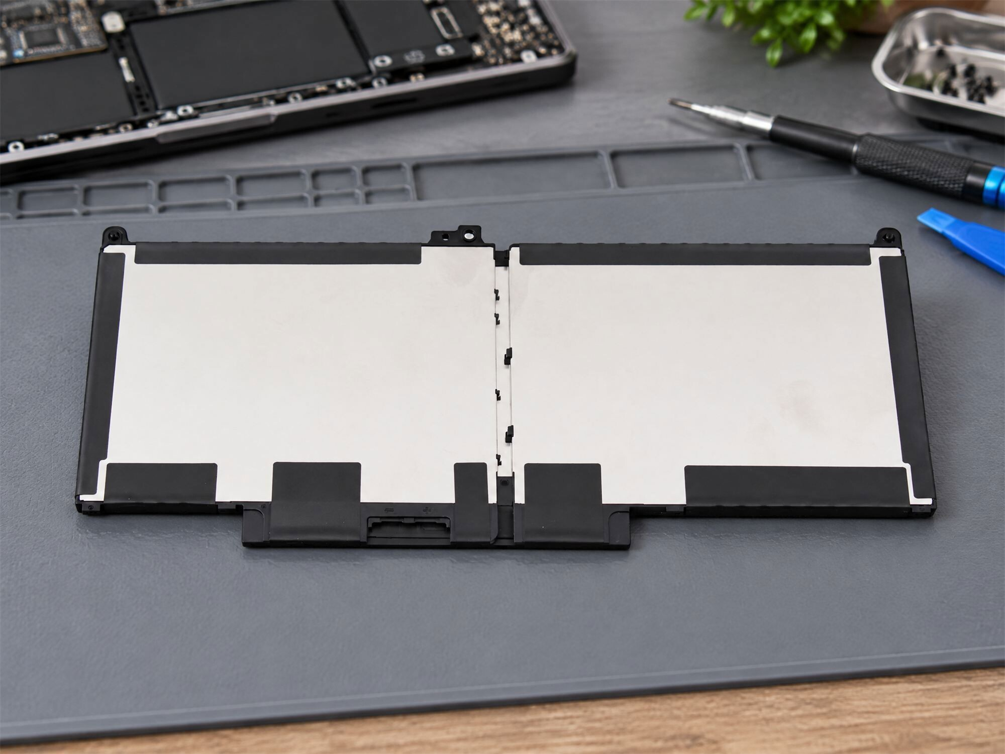 Eine Smartphone-Batterie liegt auf einer Reparaturmatte, umgeben von Werkzeugen und einem zerlegten Handy.
