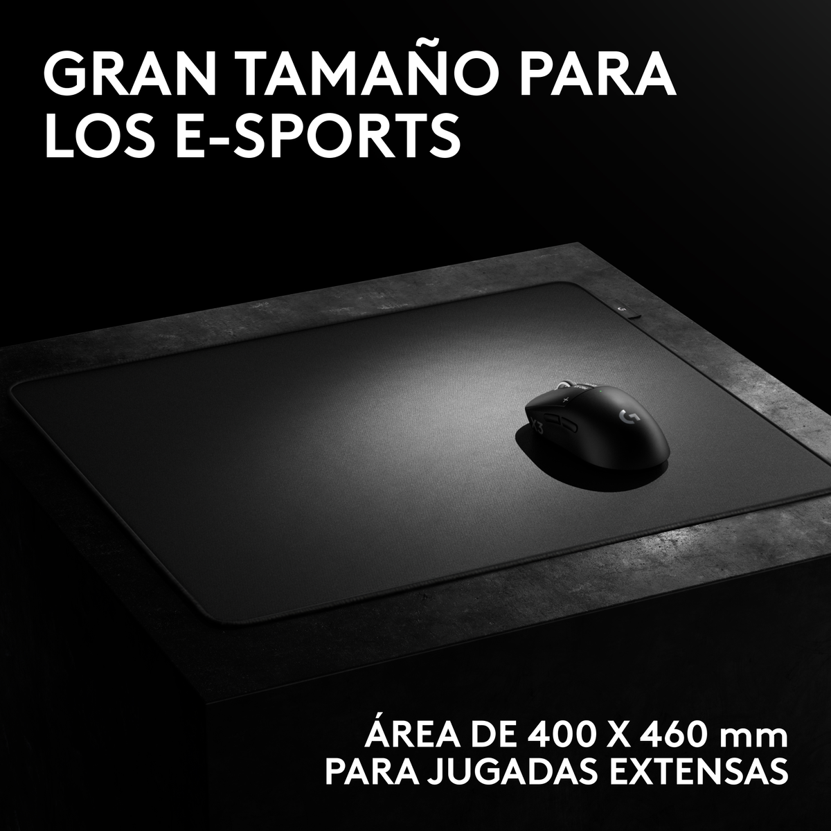 Un ratón negro para juegos en una alfombrilla negra grande sobre una superficie oscura con texto en español.
