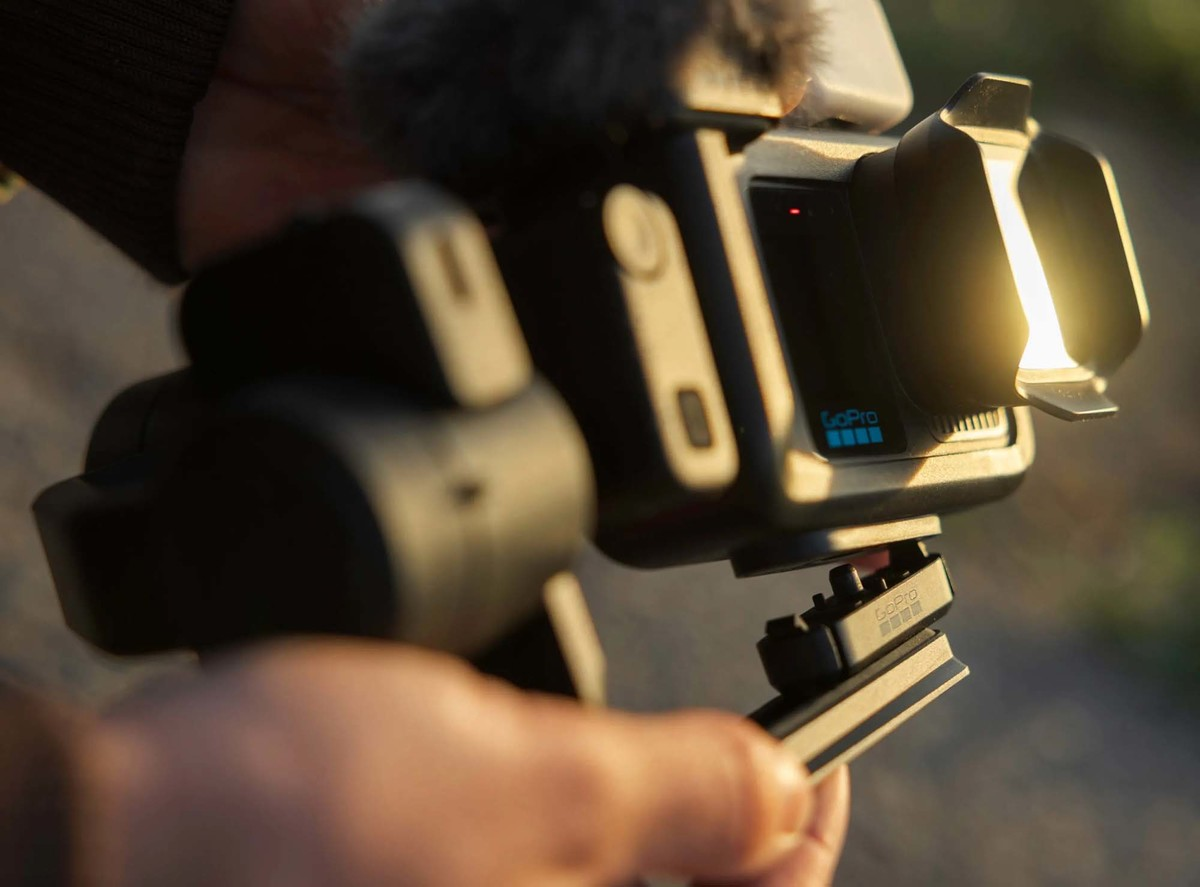 Primer plano de una persona sosteniendo una cámara GoPro montada en un estabilizador negro con luz brillante.
